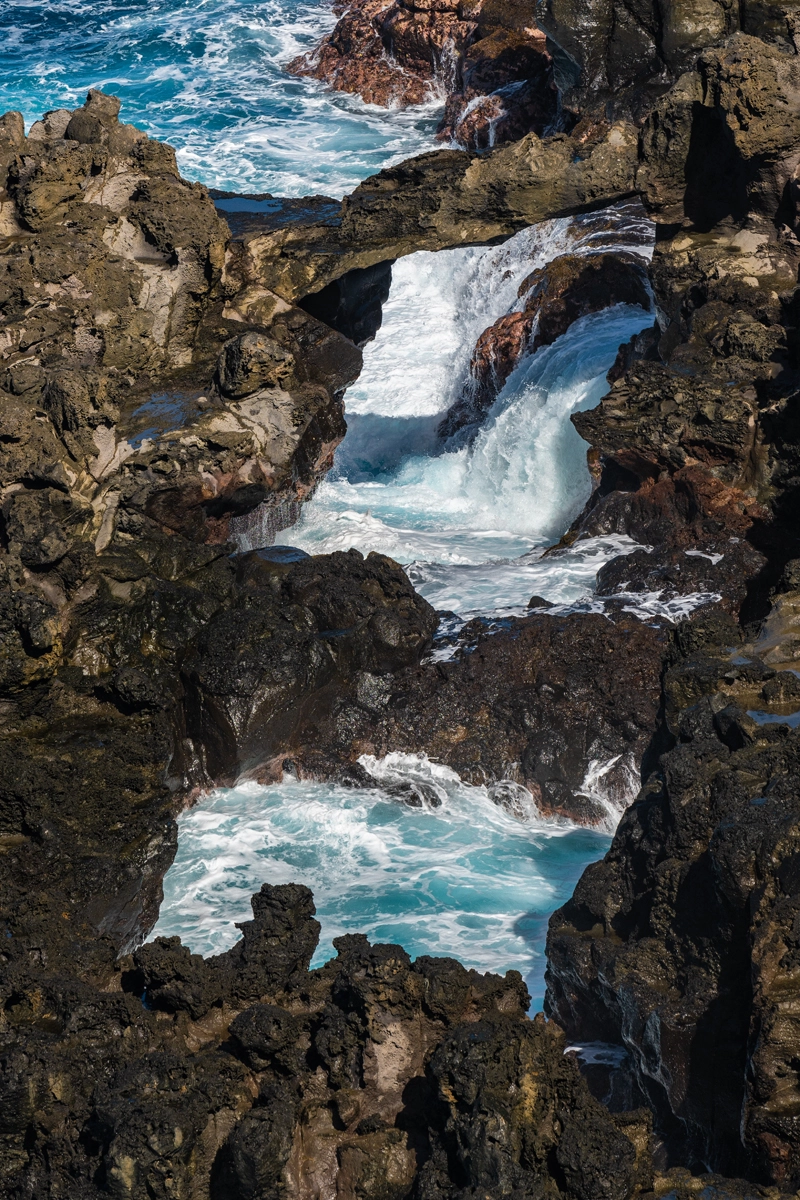 A waterfall of ocean water falling off caves formed by lava rocks