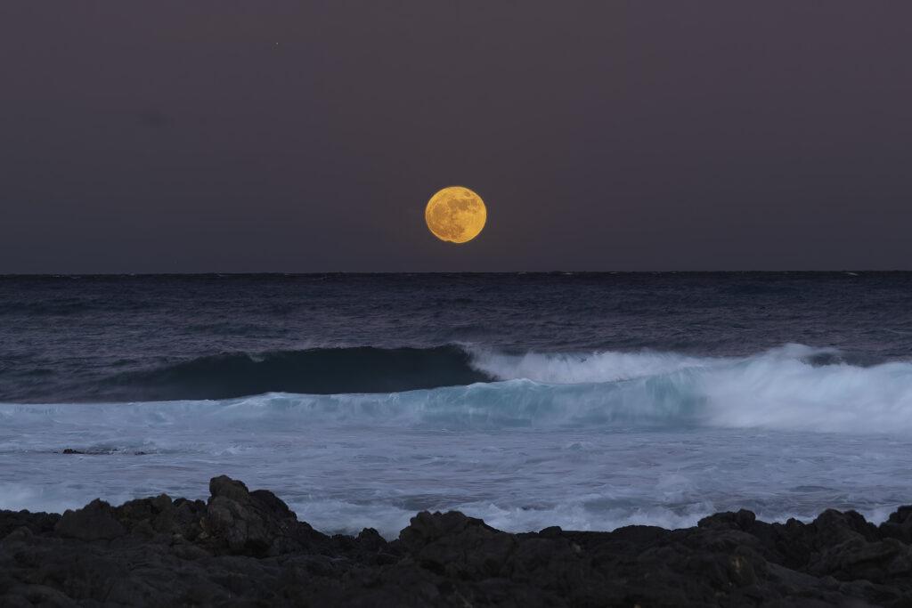 Full Moon rising in the sky above water that looks like clouds breaking on a beach in hawaii at night- Image by Raymond Enriquez Photography