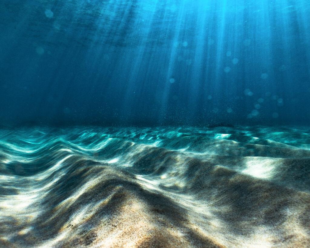 Sun ray's beaming through the surface of ocean with sand textures at the bottom of the sea.