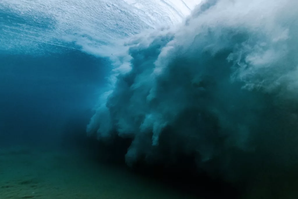 Cloud of white wash behind a breaking wave that's photographed from inside of the ocean